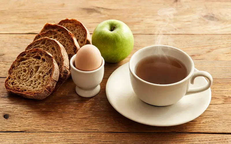Een eenvoudig ontbijt op een houten tafel: brood, een ei, een appel en thee