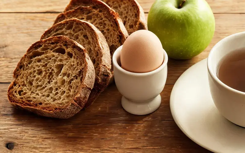 Sneden bruin brood, een gekookt ei en een groene appel op een houten tafel